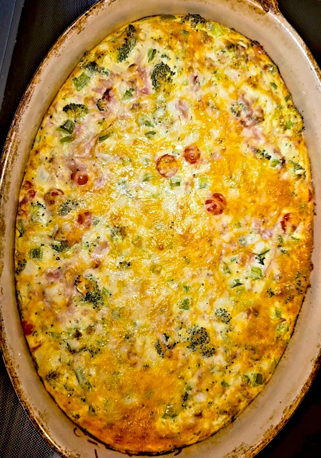 Breakfast egg bake with broccoli, ham, cherry tomatoes, and melted Colby Jack in an oval baking dish